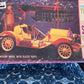 A vintage model car kit box by Stutz, featuring an illustration of a yellow 1910-style open car on a dark illustrated background. The box shows visible wear and tear, with a blue patterned fabric surface visible on the left side.