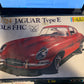 A 1:24 scale model kit box for a Jaguar Type E 318 FHC, featuring a red car illustration on the packaging, photographed next to a laptop screen.